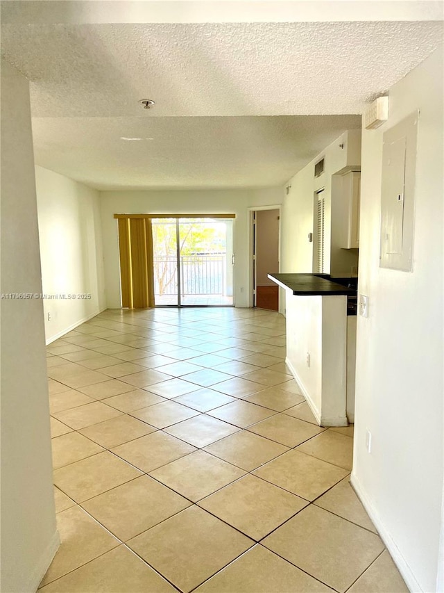 spare room featuring a textured ceiling, baseboards, light tile patterned floors, visible vents, and electric panel