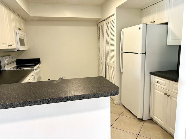 kitchen featuring dark countertops, white cabinetry, light tile patterned floors, and white appliances