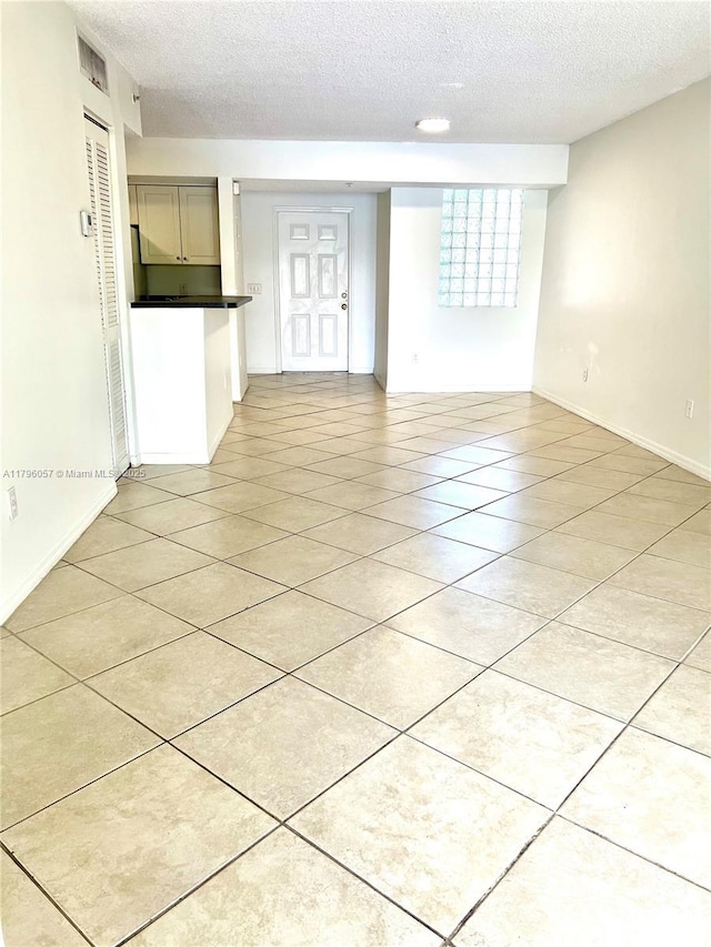 unfurnished living room featuring light tile patterned floors, baseboards, and a textured ceiling