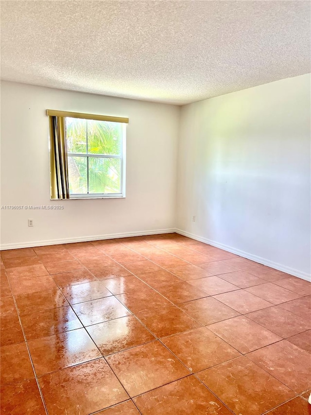 tiled spare room featuring baseboards and a textured ceiling