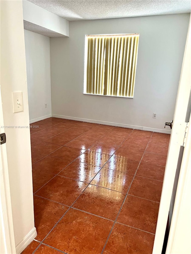 tiled spare room featuring a textured ceiling and baseboards