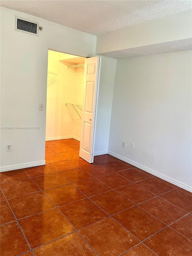 unfurnished bedroom with visible vents, a textured ceiling, baseboards, and dark tile patterned flooring
