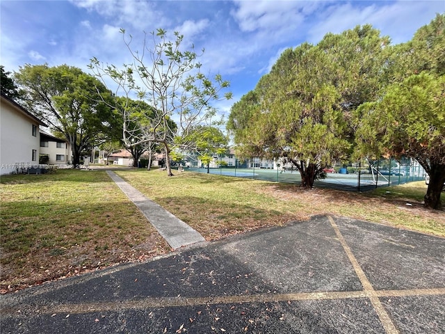 view of property's community with fence, a tennis court, a yard, and uncovered parking