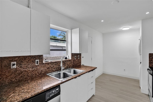 kitchen featuring dark countertops, dishwashing machine, white cabinets, a sink, and light wood-style flooring