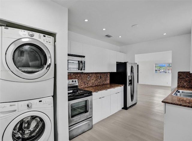 kitchen featuring dark countertops, appliances with stainless steel finishes, stacked washing maching and dryer, light wood-type flooring, and visible vents