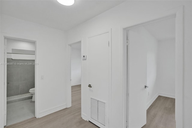 hall featuring baseboards, wood finished floors, and visible vents
