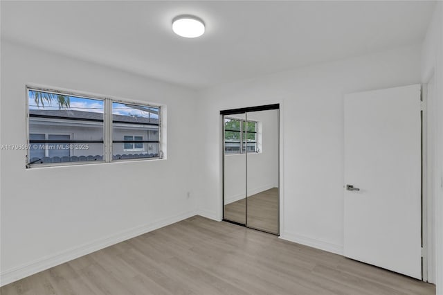 unfurnished bedroom with baseboards, a closet, and light wood-type flooring