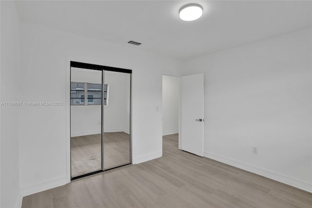 unfurnished bedroom with baseboards, a closet, wood finished floors, and visible vents