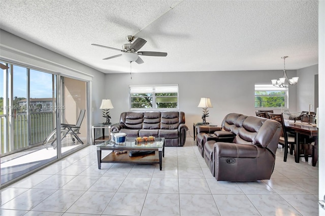 living area with light tile patterned floors, ceiling fan with notable chandelier, and a textured ceiling