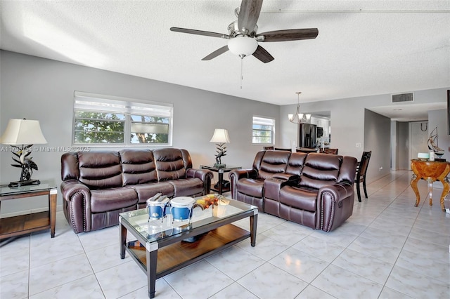 living area featuring light tile patterned flooring, a textured ceiling, visible vents, and ceiling fan with notable chandelier