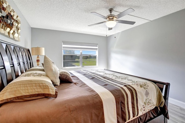 bedroom featuring baseboards, a ceiling fan, a textured ceiling, and wood finished floors