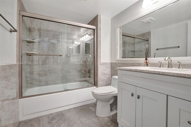full bath featuring tile walls, vanity, toilet, shower / bath combination with glass door, and marble finish floor