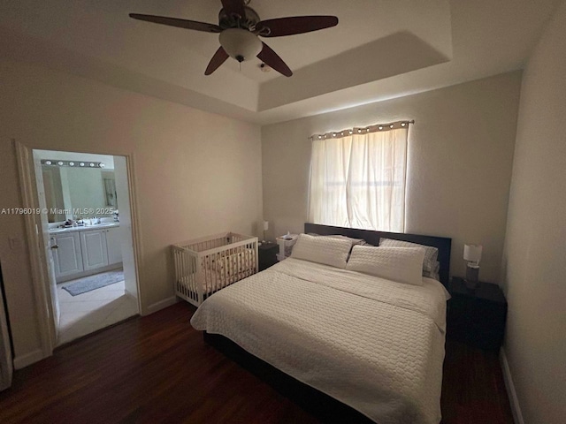 bedroom featuring wood finished floors, baseboards, connected bathroom, a raised ceiling, and a ceiling fan