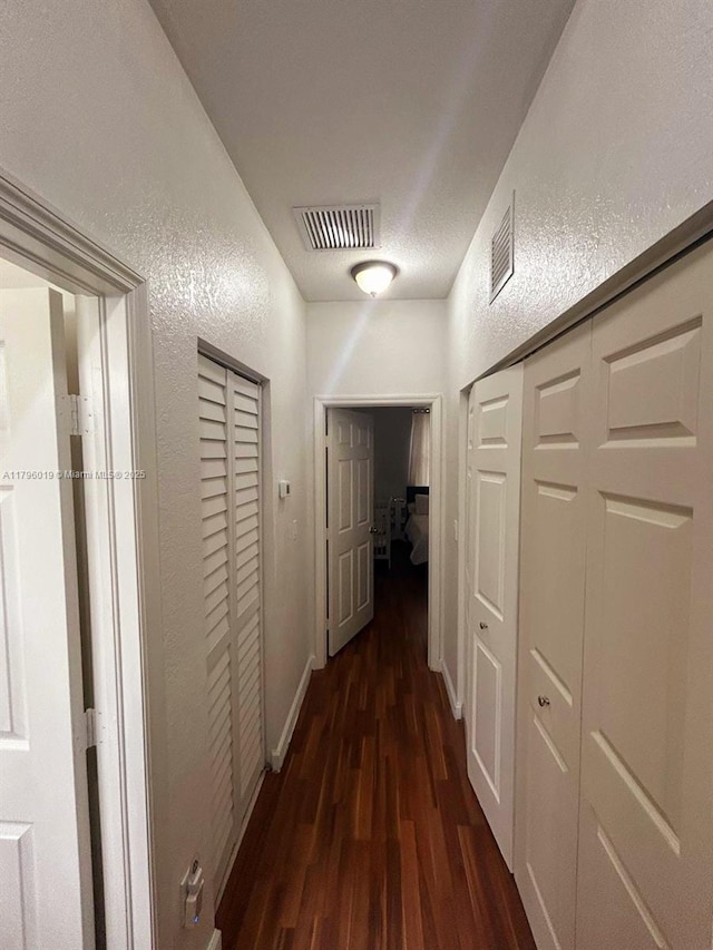 hall with baseboards, a textured wall, wood finished floors, and visible vents