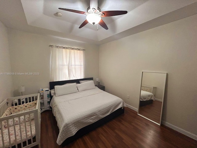 bedroom featuring baseboards, a ceiling fan, a tray ceiling, and wood finished floors
