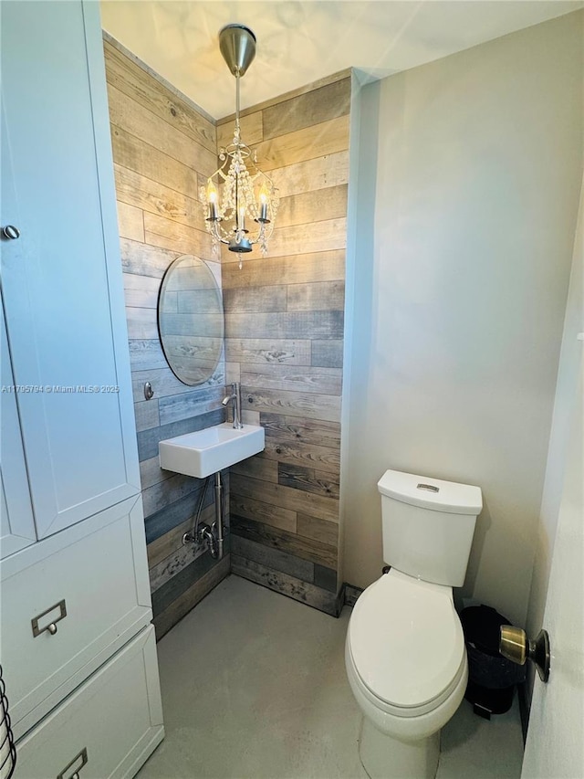 bathroom featuring a sink, concrete flooring, wooden walls, and toilet