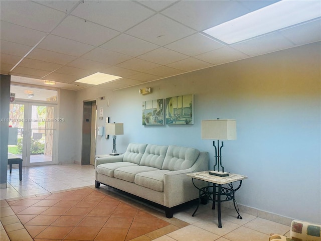 living room featuring baseboards, a drop ceiling, and light tile patterned flooring