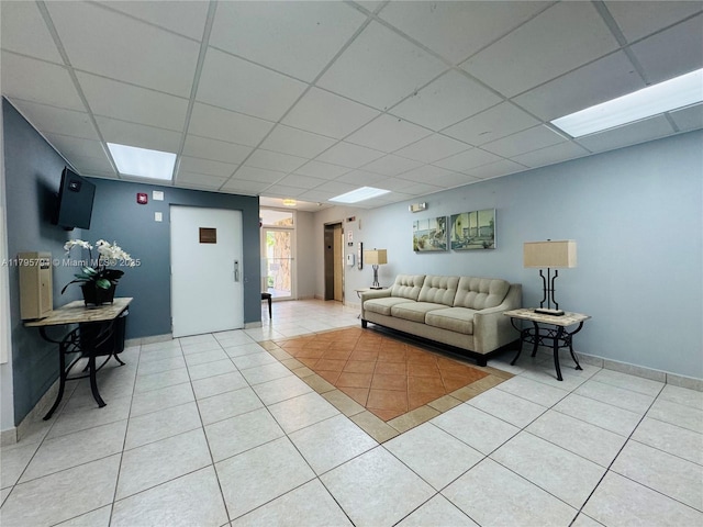 living area featuring light tile patterned floors, baseboards, and a drop ceiling