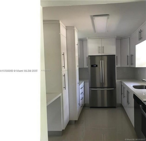 kitchen featuring a sink, light countertops, stainless steel refrigerator, and white cabinets