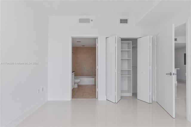 unfurnished bedroom featuring visible vents, ensuite bathroom, tile patterned flooring, and a closet