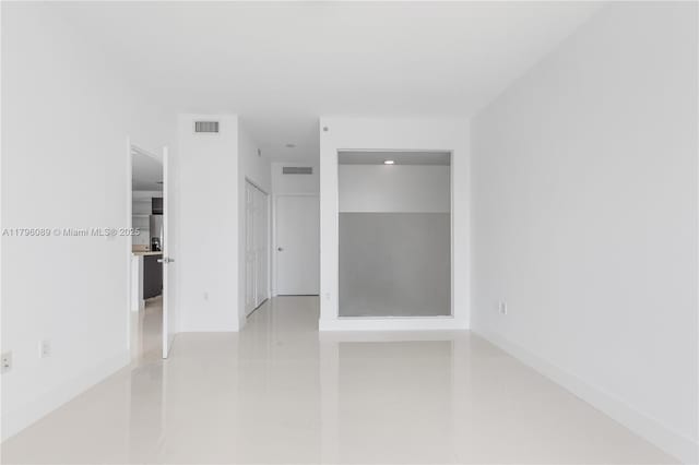 tiled empty room featuring baseboards and visible vents