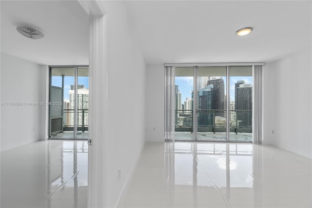 tiled empty room with plenty of natural light, a view of city, floor to ceiling windows, and baseboards