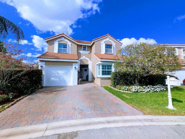 mediterranean / spanish-style home featuring a tile roof, decorative driveway, a front lawn, an attached garage, and stucco siding