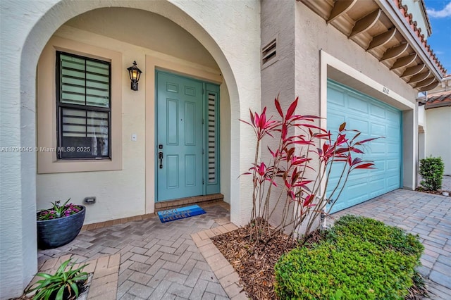 view of exterior entry featuring visible vents, stucco siding, and driveway