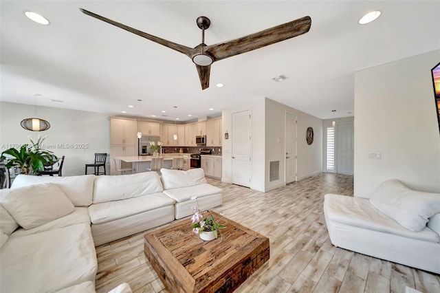 living room with light wood-type flooring, recessed lighting, ceiling fan, and visible vents