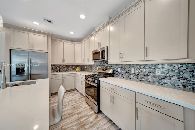 kitchen with light wood-style floors, light countertops, stainless steel appliances, backsplash, and visible vents