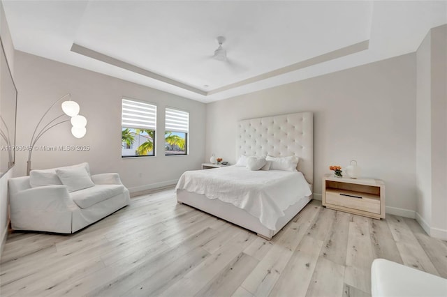 bedroom with a ceiling fan, baseboards, a raised ceiling, and light wood-type flooring