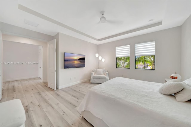 bedroom featuring a tray ceiling, ceiling fan, baseboards, and light wood finished floors