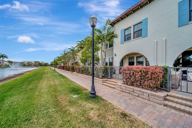 view of property exterior featuring fence, stucco siding, a lawn, a water view, and a tile roof