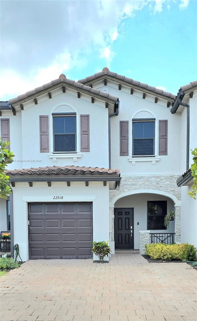 view of front of house with stone siding, decorative driveway, stucco siding, an attached garage, and a tile roof