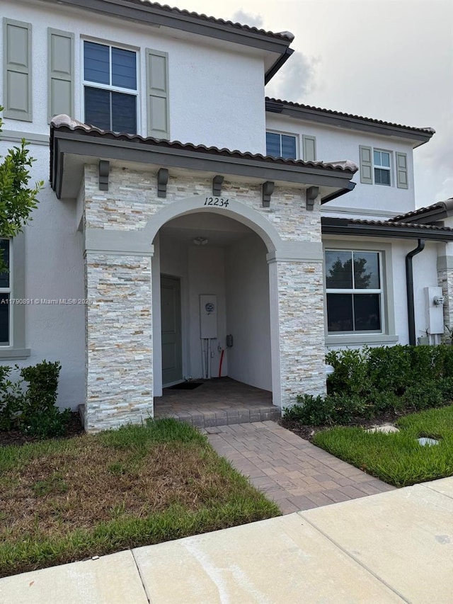 view of front of house featuring a tile roof, stone siding, and stucco siding