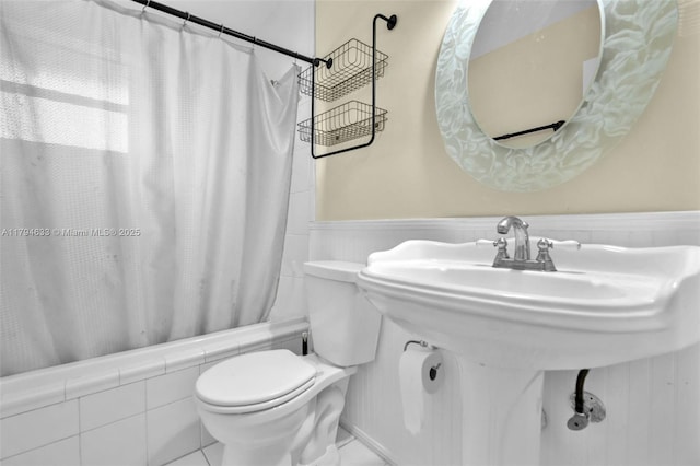 full bath featuring shower / tub combo with curtain, a wainscoted wall, and toilet
