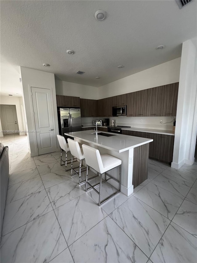 4409 SW 173rd Ave, Miramar, FL 33029 - kitchen with modern cabinets, appliances with stainless steel finishes, light marble finish flooring, a breakfast bar area, and a textured ceiling