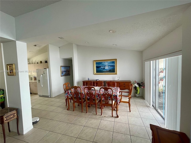 dining space with a textured ceiling, light tile patterned floors, and lofted ceiling