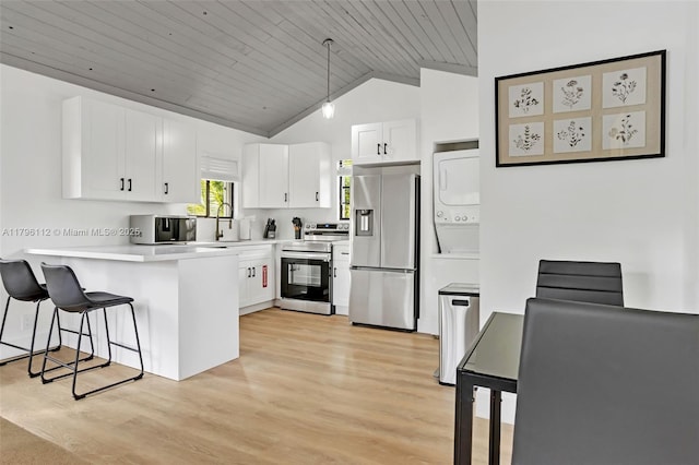 kitchen featuring a peninsula, stacked washer / dryer, a breakfast bar area, appliances with stainless steel finishes, and vaulted ceiling