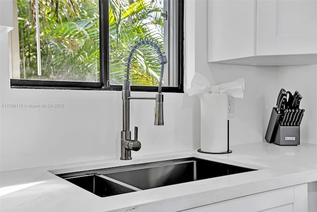 details with white cabinetry, light stone countertops, and a sink