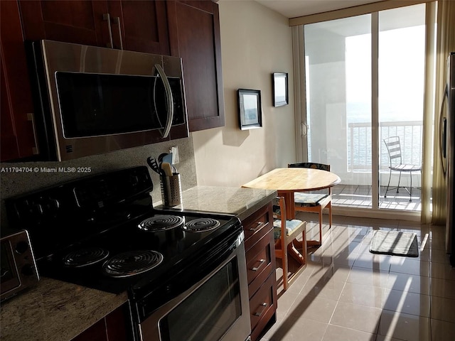 kitchen featuring electric range, light tile patterned flooring, dark brown cabinets, stainless steel microwave, and backsplash