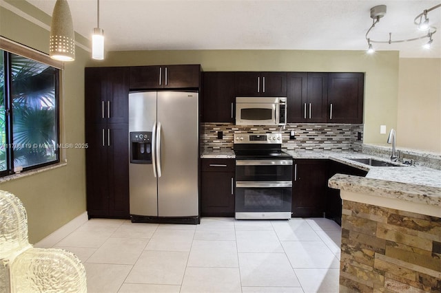kitchen featuring dark brown cabinets, light stone counters, a sink, appliances with stainless steel finishes, and backsplash