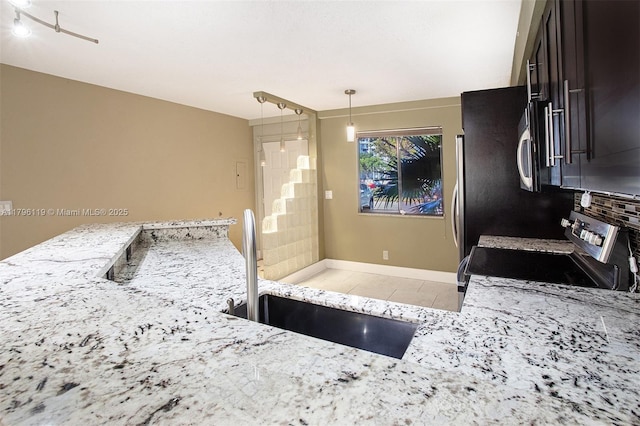 kitchen with appliances with stainless steel finishes, hanging light fixtures, light stone countertops, a sink, and light tile patterned floors