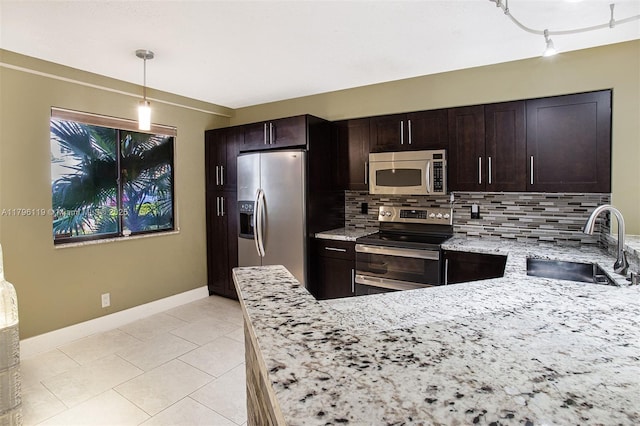 kitchen with light stone countertops, appliances with stainless steel finishes, a sink, baseboards, and backsplash