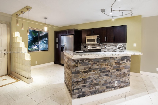 kitchen with backsplash, appliances with stainless steel finishes, hanging light fixtures, light tile patterned floors, and light stone counters