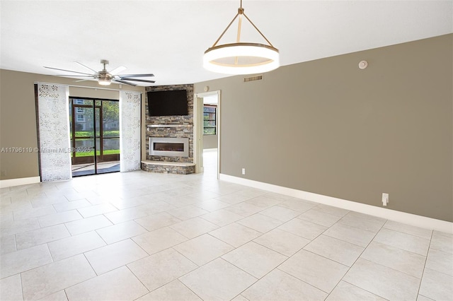 unfurnished living room with a stone fireplace, baseboards, ceiling fan, and visible vents