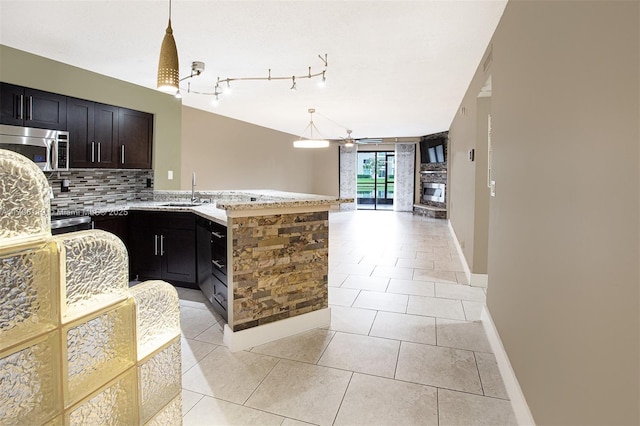 kitchen featuring decorative backsplash, a peninsula, open floor plan, stainless steel microwave, and a sink