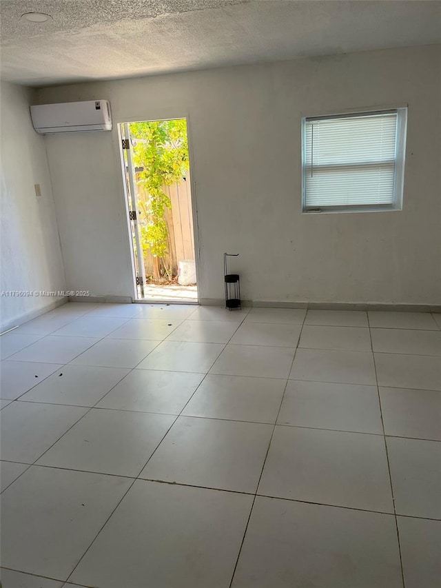 tiled empty room featuring a textured ceiling and a wall mounted air conditioner