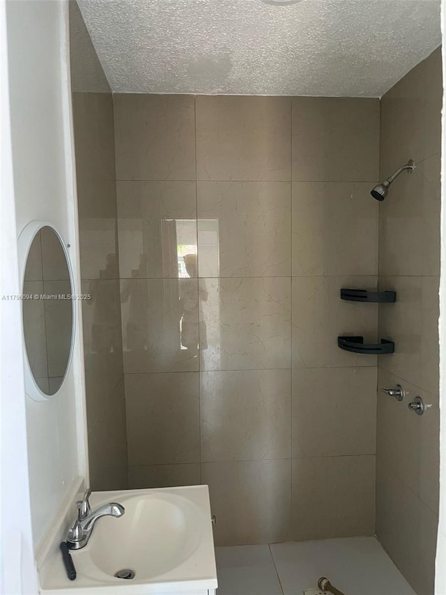 full bathroom with a textured ceiling, a tile shower, and a sink