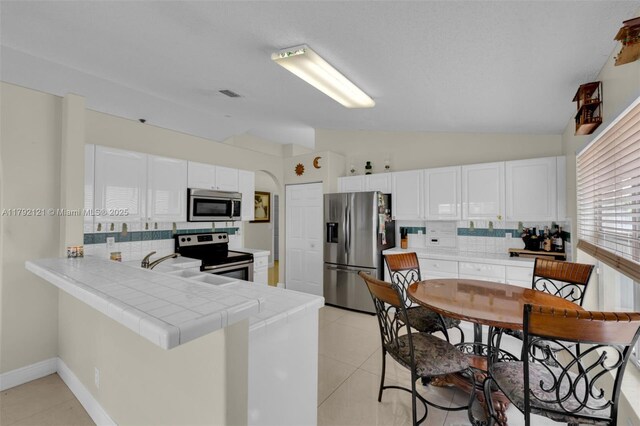 18271 SW 27th St, Miramar, FL 33029 - kitchen featuring appliances with stainless steel finishes, tile countertops, lofted ceiling, tasteful backsplash, and a peninsula